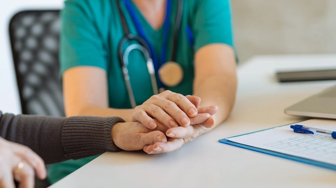 Healthcare professional holding the hands of an elder patient
