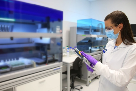 Scientist in mask and gloves using tablet in laboratory