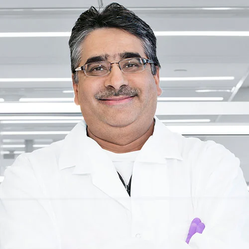 Foto de retrato de um homem, mais velho, pardo, com cabelo curto liso, grisalho nas laterais e preto no topo, de óculos e bigode, com sorriso para a câmera, trajado de jaleco. 